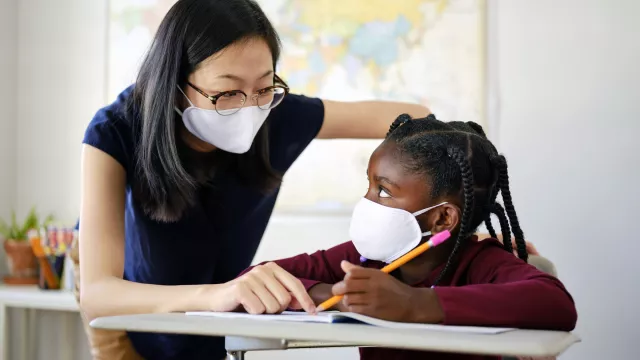 A masked teacher and student working together on a lesson.